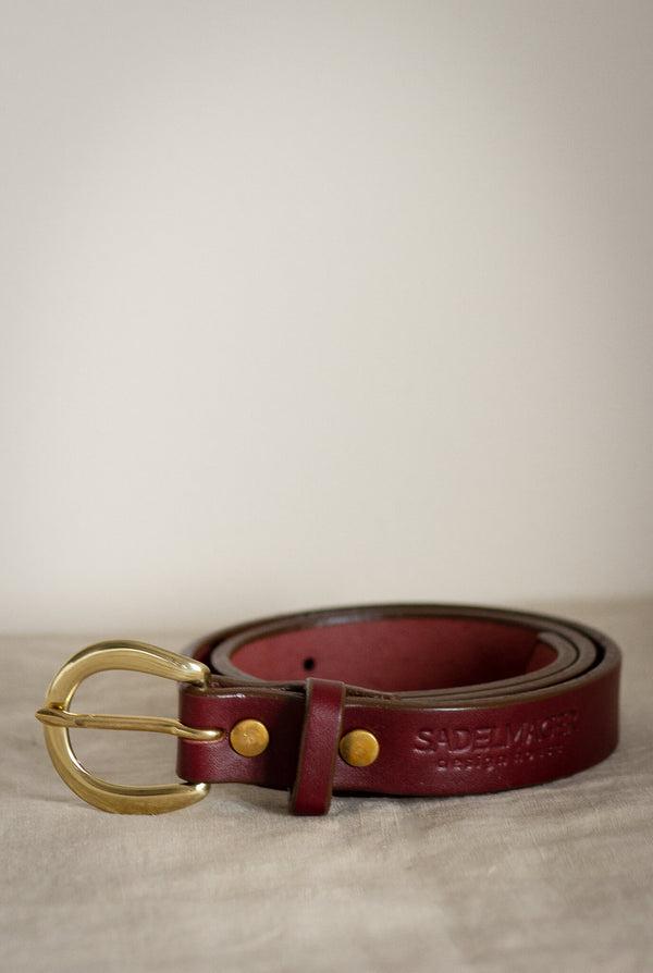 the noriker leather belt made in canada seen here on a white backdrop in red oxblood leather and solid brass hardware made in canada