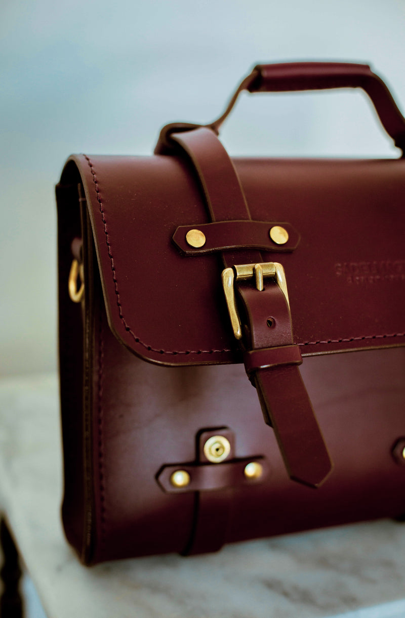 close up of left side oldenburg small leather messenger bag in oxblood with brass buckles  