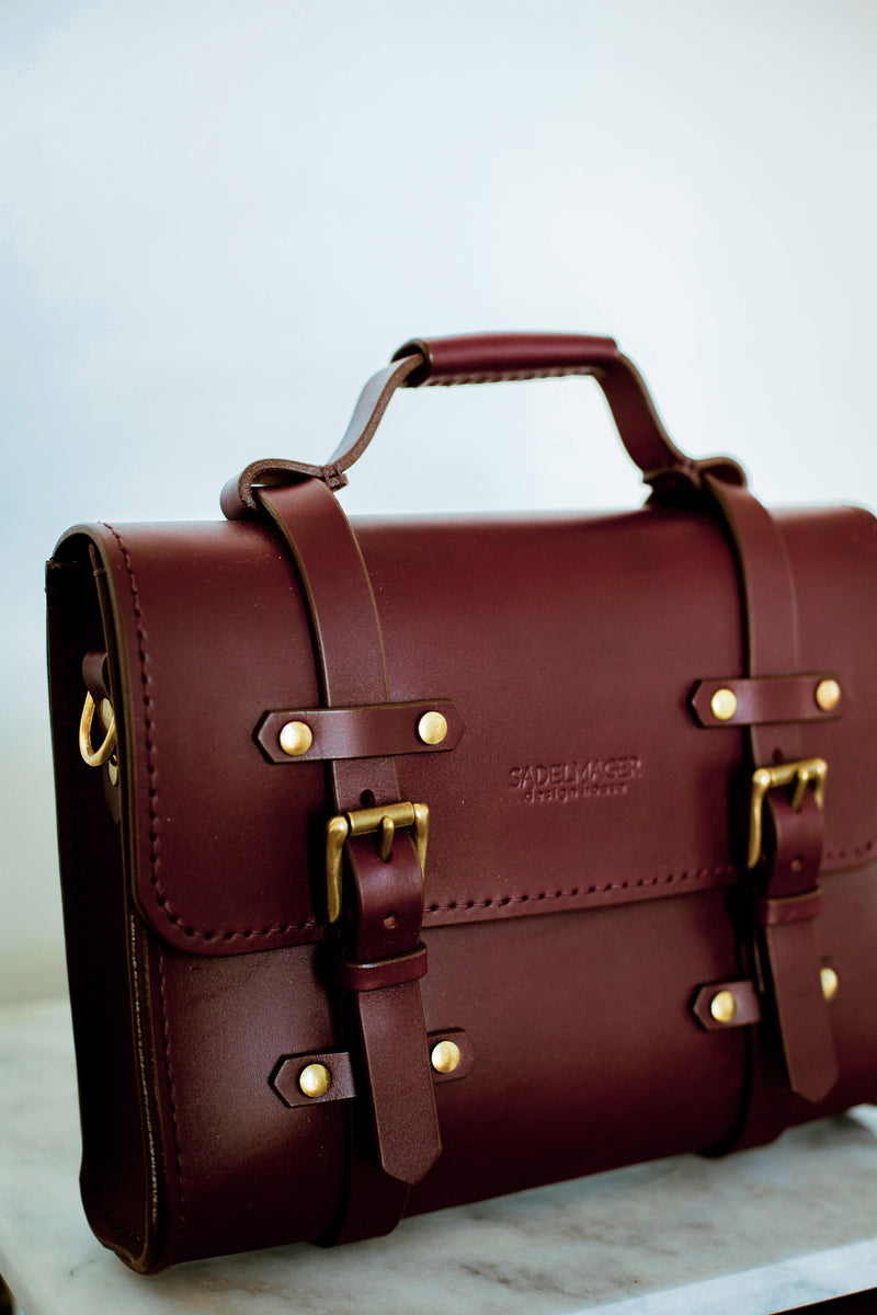 left angle close up of oldenburg small leather messenger bag in oxblood with brass buckles  