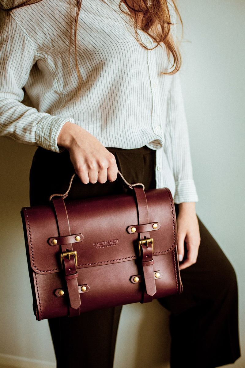 model holding oldenburg small leather messenger bag in oxblood with brass buckles  