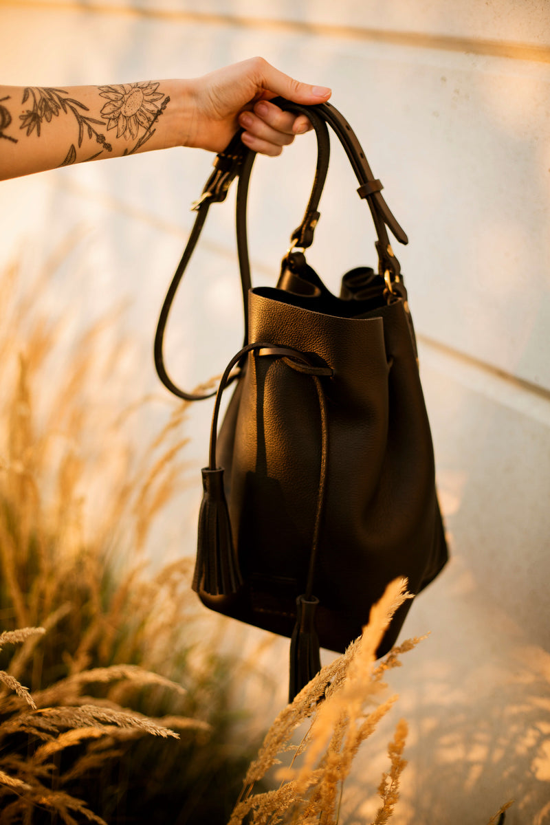 black leather suede bucket bag with solid brass and tassels worn crossbody fits lots of items and is made in Canada
